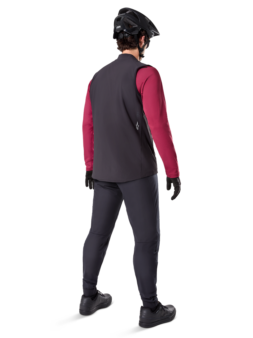 Alpinestars Gilet Termico A-Dura, gilet da ciclismo nero, mostrato dal retro su un modello che indossa una maglia a maniche lunghe bordeaux e pantaloni da ciclismo neri, abbinato a casco e guanti da mountain bike neri, abbigliamento tecnico per il freddo