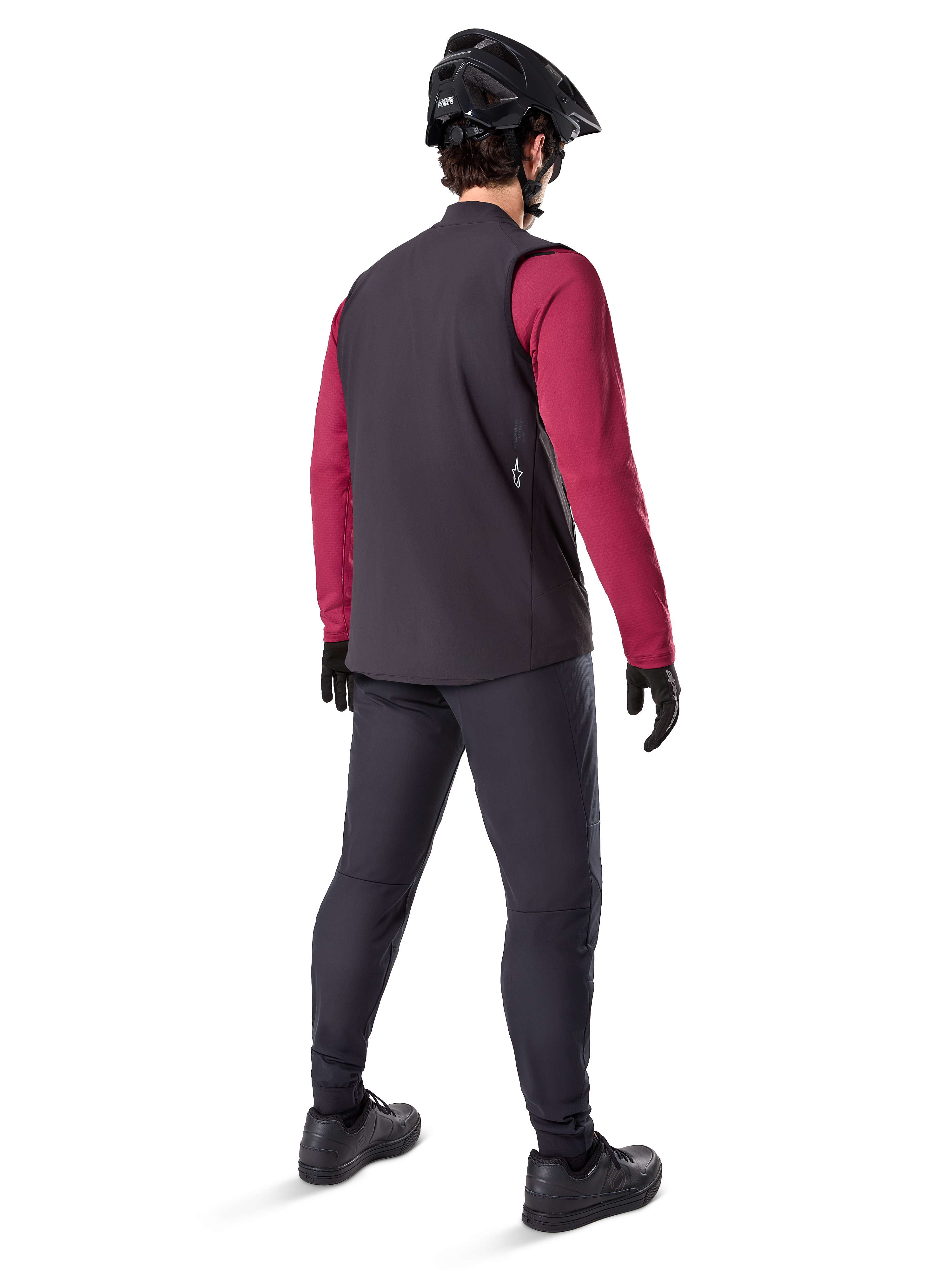 Alpinestars Gilet Termico A-Dura, gilet da ciclismo nero, mostrato dal retro su un modello che indossa una maglia a maniche lunghe bordeaux e pantaloni da ciclismo neri, abbinato a casco e guanti da mountain bike neri, abbigliamento tecnico per il freddo