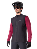 Alpinestars A-Dura Thermal Vest, gilet termico nero da ciclismo, indossato sopra una maglia bordeaux a maniche lunghe, con logo bianco sul petto, abbinato a un casco da MTB nero e occhiali da sole, strato isolante performante per mountain bike