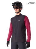 Alpinestars Gilet Termico A-Dura, gilet termico da mountain bike da uomo in nero, indossato da un modello con casco e maglia a maniche lunghe rossa, isolamento per la guida MTB in climi freddi