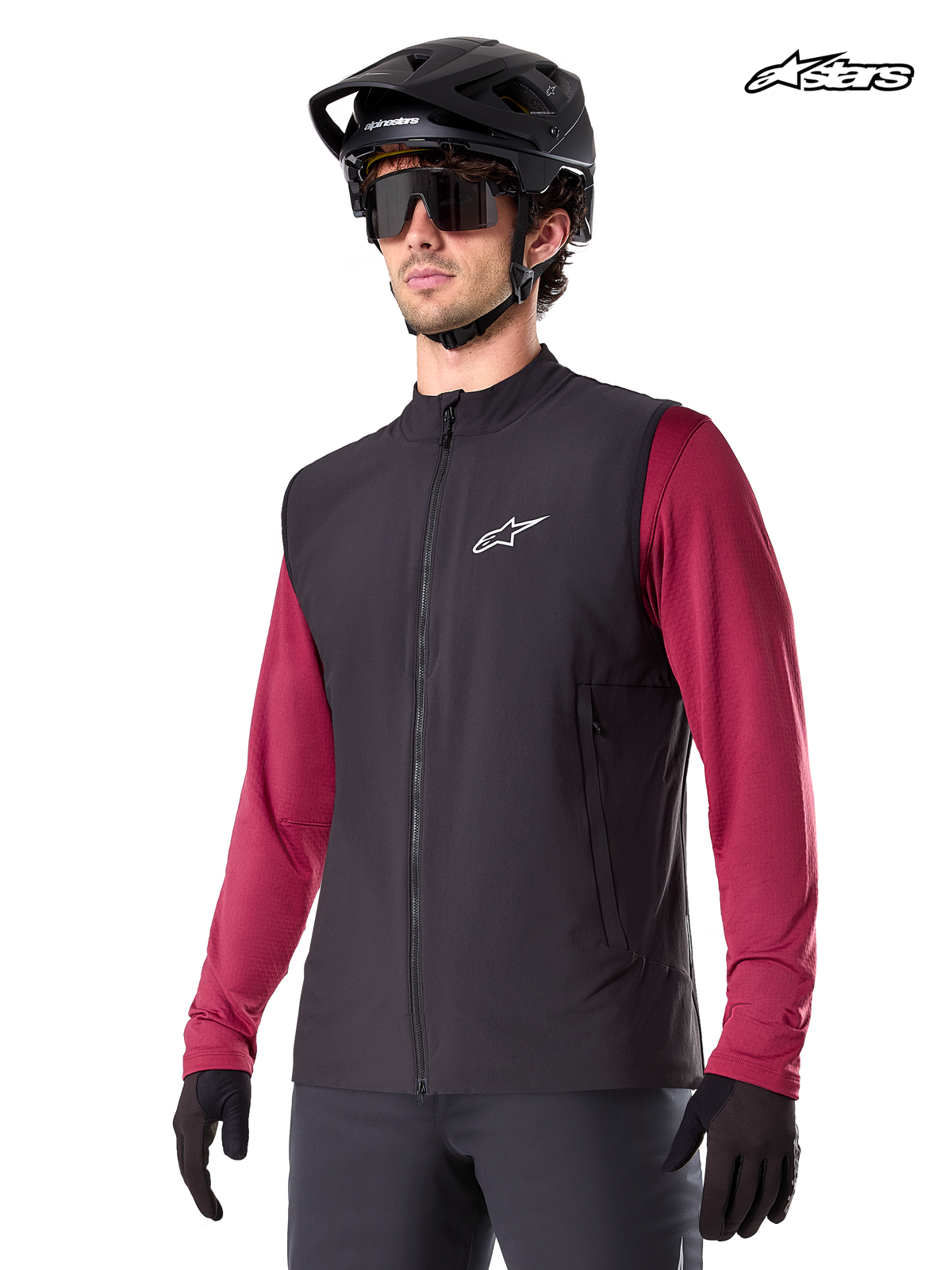 Alpinestars Gilet Termico A-Dura, gilet termico da mountain bike da uomo in nero, indossato da un modello con casco e maglia a maniche lunghe rossa, isolamento per la guida MTB in climi freddi