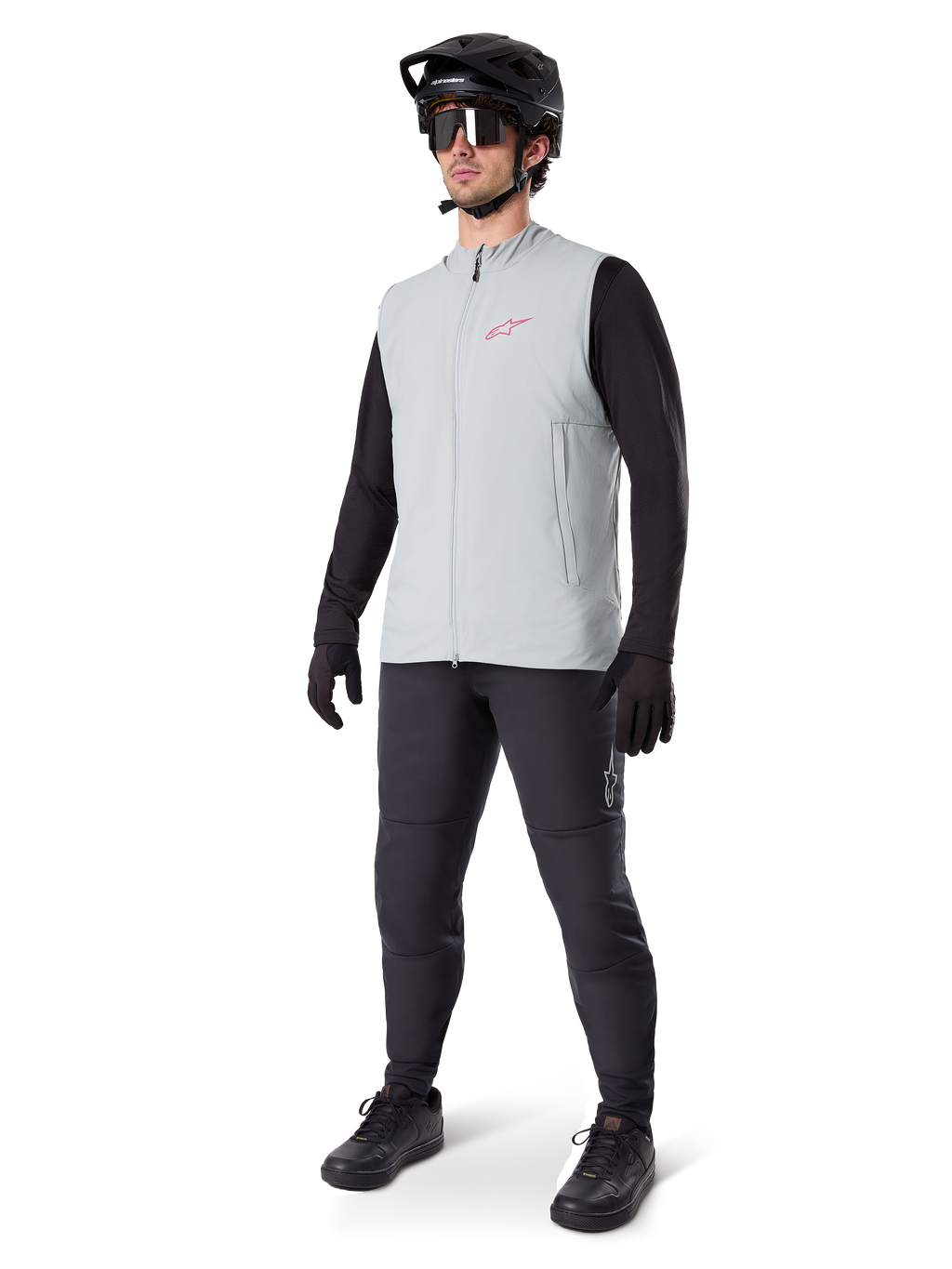 Alpinestars Gilet Termico A-Dura, gilet da ciclismo grigio titanio con logo rosa, indossato da un modello con maglia nera a maniche lunghe, pantaloni grigio scuro e casco da mountain bike nero, equipaggiamento tecnico per il freddo