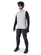 Alpinestars Gilet Termico A-Dura, gilet da ciclismo grigio titanio con logo rosa, indossato da un modello con maglia nera a maniche lunghe, pantaloni grigio scuro e casco da mountain bike nero, equipaggiamento tecnico per il freddo