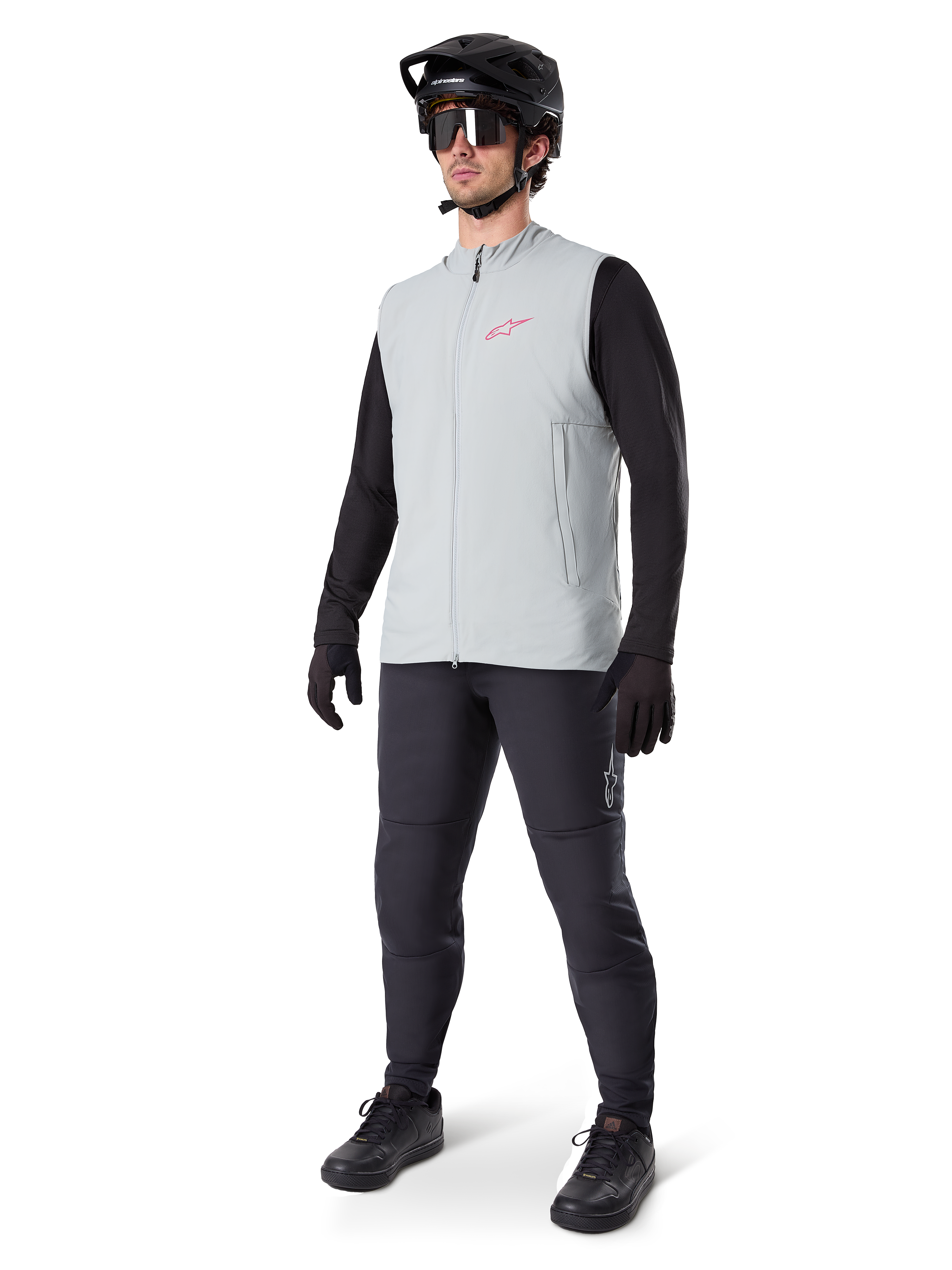 Alpinestars Gilet Termico A-Dura, gilet da ciclismo grigio titanio con logo rosa, indossato da un modello con maglia nera a maniche lunghe, pantaloni grigio scuro e casco da mountain bike nero, equipaggiamento tecnico per il freddo