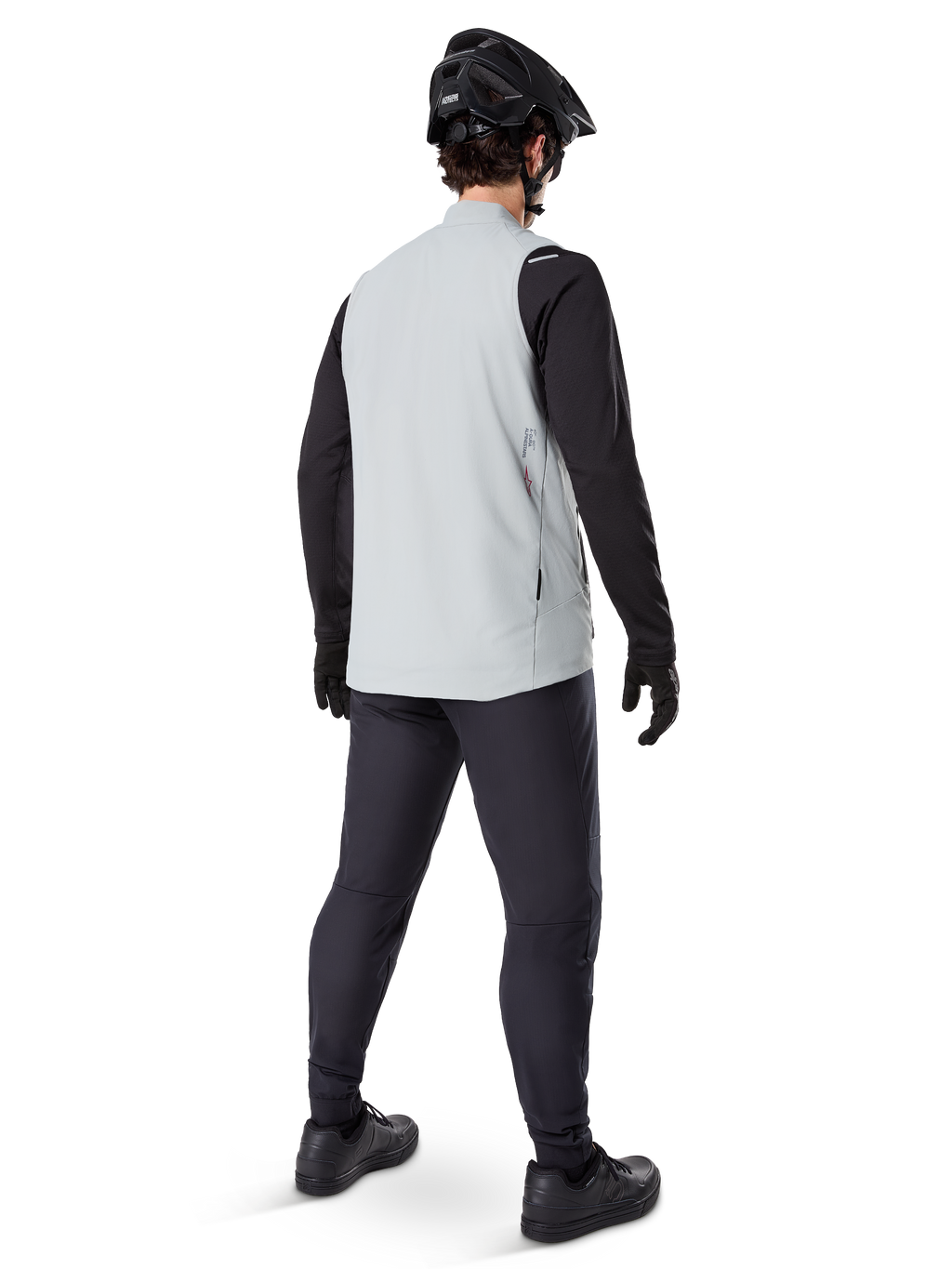 Alpinestars A-Dura Thermal Vest, grigio titanio, vista posteriore del modello che indossa il gilet da ciclismo isolato sopra una maglia nera a maniche lunghe e pantaloni scuri, completo di casco da mountain bike e guanti neri, progettato per la guida fuoristrada in condizioni fredde