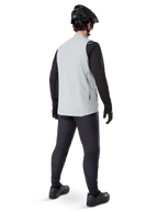 Alpinestars A-Dura Thermal Vest, grigio titanio, vista posteriore del modello che indossa il gilet da ciclismo isolato sopra una maglia nera a maniche lunghe e pantaloni scuri, completo di casco da mountain bike e guanti neri, progettato per la guida fuoristrada in condizioni fredde