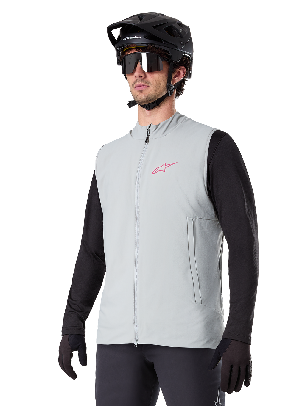 Alpinestars A-Dura Thermal Vest, grigio titanio, gilet termico da ciclismo, indossato sopra una maglia nera a maniche lunghe con casco da mountain bike e guanti neri, con logo rosa sul petto e tasche laterali verticali con zip