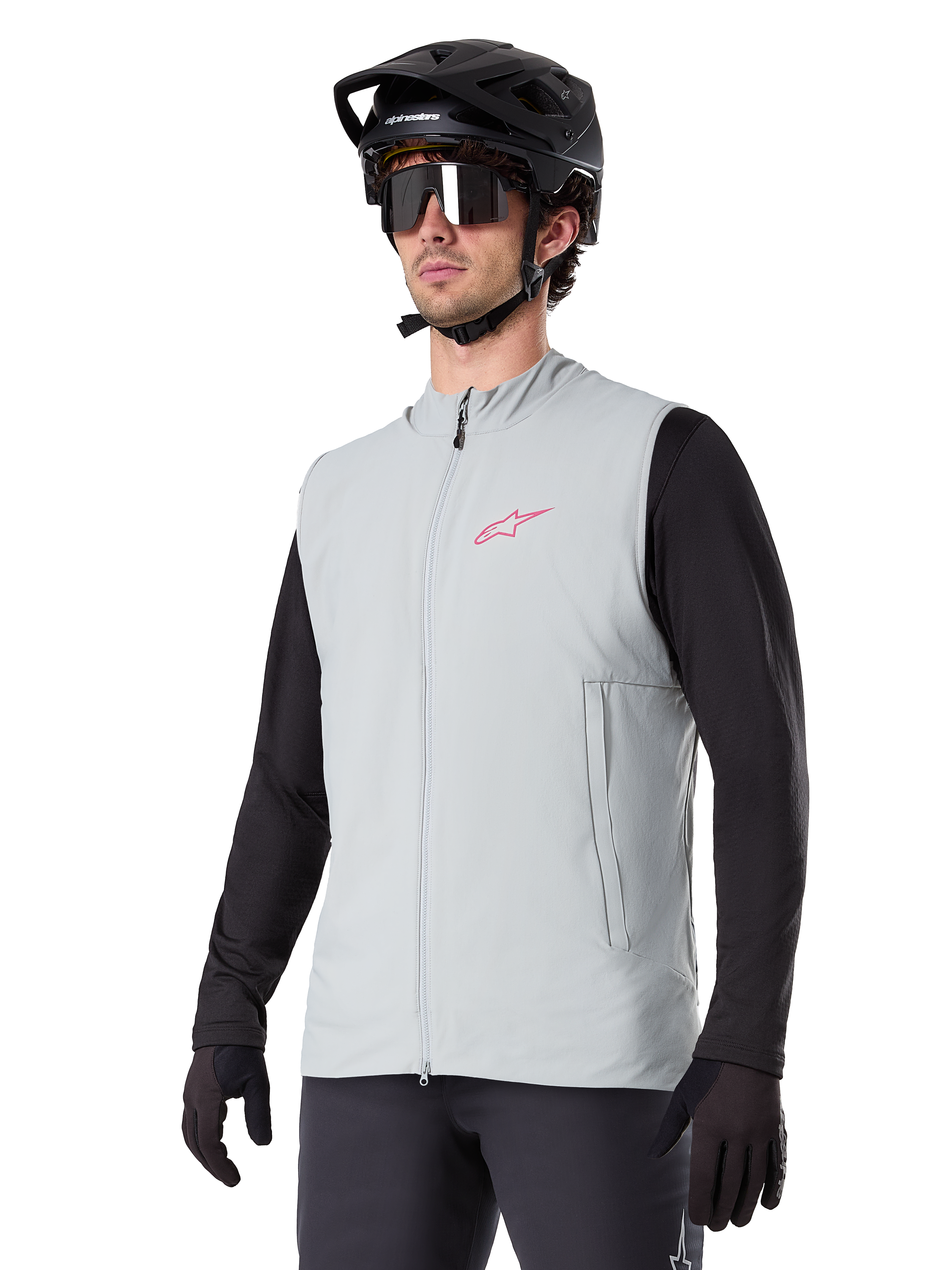 Alpinestars A-Dura Thermal Vest, grigio titanio, gilet termico da ciclismo, indossato sopra una maglia nera a maniche lunghe con casco da mountain bike e guanti neri, con logo rosa sul petto e tasche laterali verticali con zip
