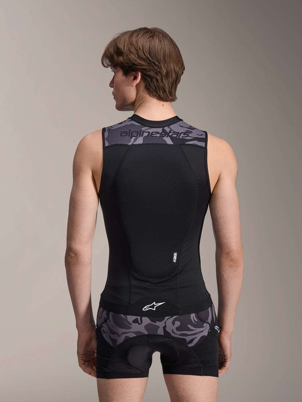 Gilet protettivo Alpinestars A-Motion Plasma, Black Camo, vista posteriore su modello uomo, con costruzione in mesh traspirante, paraschiena Nucleon Plasma integrato, dettagli mimetici grigi su spalle e vita e logo Alpinestars.
