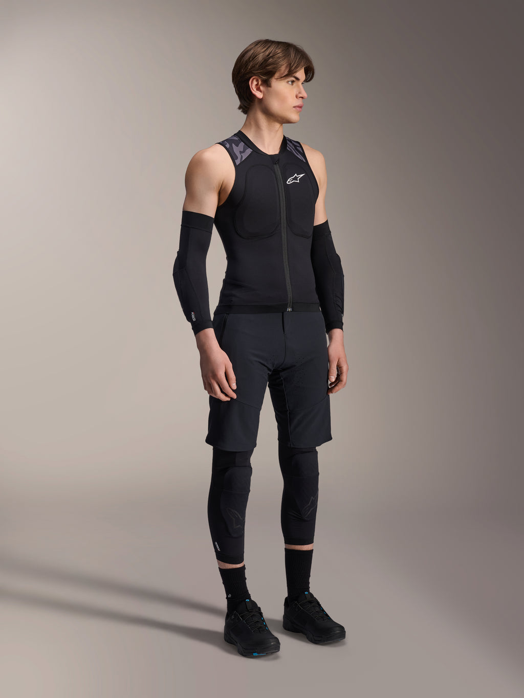 Alpinestars A-Motion Plasma Protection Vest, gilet protettivo da MTB senza maniche nero e camo, vista a figura intera del modello con maniche protettive e ginocchiere, zip frontale con logo Alpinestars bianco, attrezzatura tecnica per mountain bike