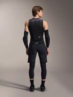Gilet protettivo Alpinestars A-Motion Plasma, vista posteriore, nero con accenti mimetici grigi sulle spalle, indossato da un modello con gomitiere nere, pantaloncini da ciclismo sopra leggings e scarpe da ciclismo nere, che mostra il paraschiena integrato