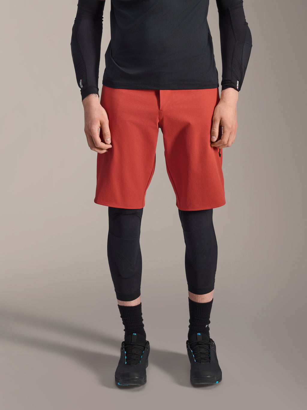 Alpinestars A-Motion Plasma Knee Sleeve, ginocchiera da MTB nera, indossata con pantaloncini rossi e maglia nera a maniche lunghe, design ergonomico dal profilo sottile, struttura in mesh leggero per la guida fuoristrada