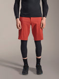 Alpinestars A-Motion Plasma Knee Sleeve, ginocchiera da MTB nera, indossata con pantaloncini rossi e maglia nera a maniche lunghe, design ergonomico dal profilo sottile, struttura in mesh leggero per la guida fuoristrada