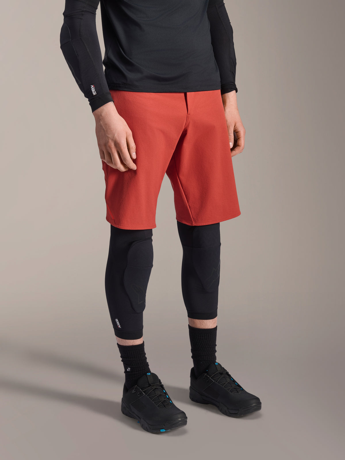Alpinestars A-Motion Plasma Knee Sleeve, ginocchiera MTB, nero, indossata con pantaloncini rossi e scarpe da mountain bike nere, design slip-on a basso profilo con imbottiture protettive sagomate e mesh traspirante