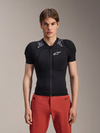 Modello che indossa la giacca protettiva Alpinestars A-Motion Plasma - Short Sleeve, nera con imbottitura mimetica grigia sulle spalle, logo Alpinestars bianco sul petto, abbinata a pantaloni rossi, protezione per il corpo MTB slim-fit con zip frontale