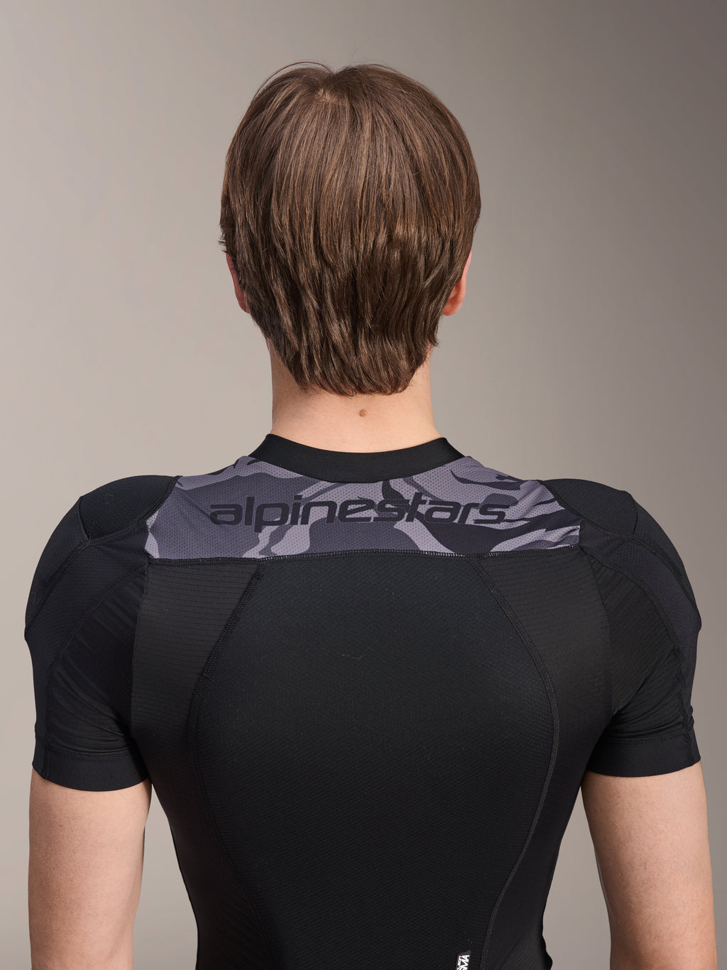 Alpinestars A-Motion Plasma Protection Jacket - Manica Corta, vista posteriore della parte superiore del busto, nero con pannello camo grigio sulle spalle e logo Alpinestars, struttura in mesh elasticizzato traspirante per protezione MTB