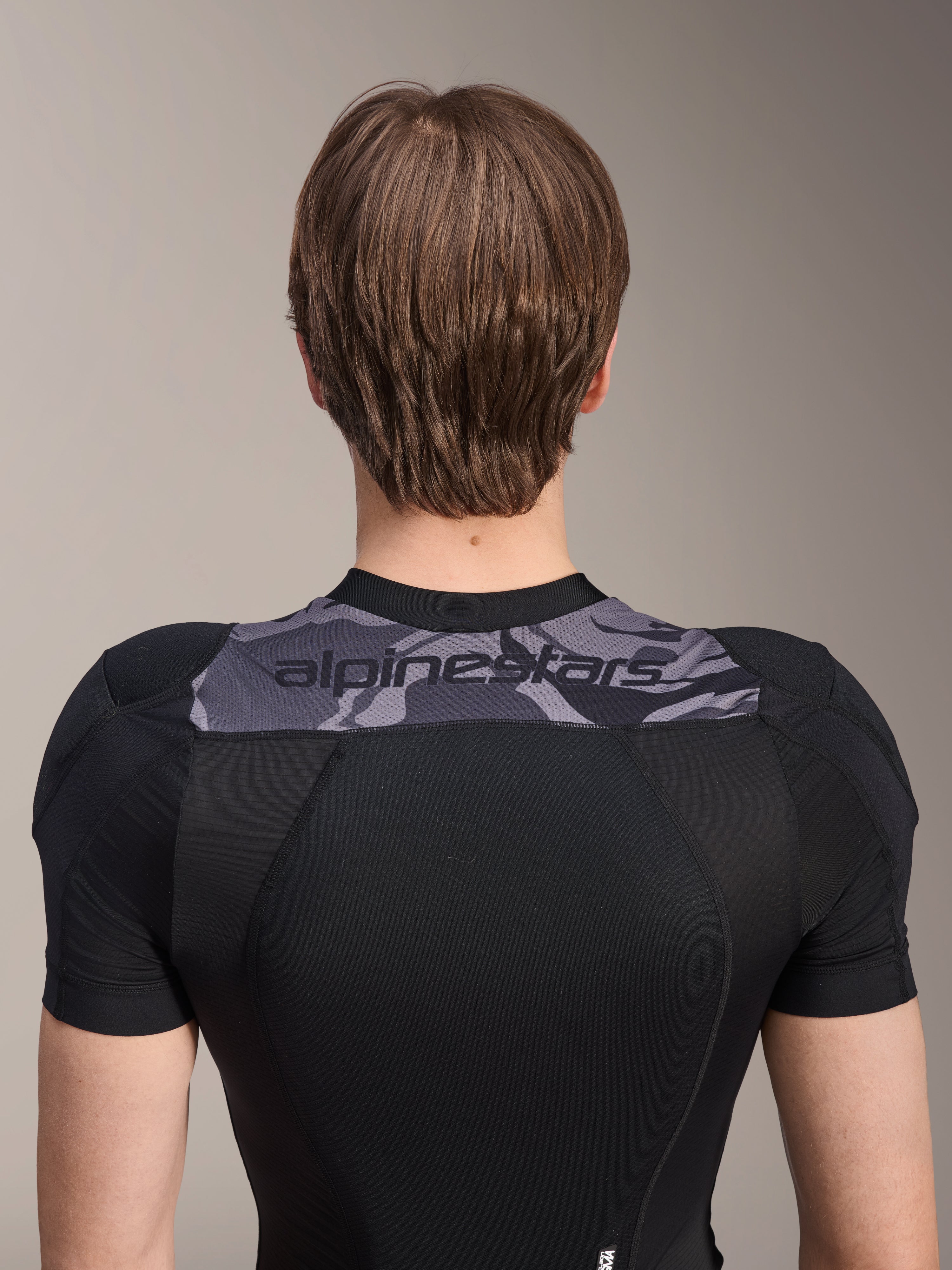 Alpinestars A-Motion Plasma Protection Jacket - Manica Corta, vista posteriore della parte superiore del busto, nero con pannello camo grigio sulle spalle e logo Alpinestars, struttura in mesh elasticizzato traspirante per protezione MTB
