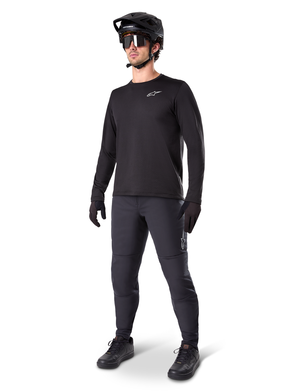 Ciclista di mountain bike che indossa i Pantaloni Termici Alpinestars A-Dura, nero, abbinati a una maglia a maniche lunghe nera, casco nero e occhiali da sole, con logo Alpinestars argento sulla coscia sinistra, progettati per il trail riding in climi freddi