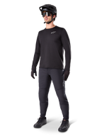 Ciclista di mountain bike che indossa i Pantaloni Termici Alpinestars A-Dura, nero, abbinati a una maglia a maniche lunghe nera, casco nero e occhiali da sole, con logo Alpinestars argento sulla coscia sinistra, progettati per il trail riding in climi freddi