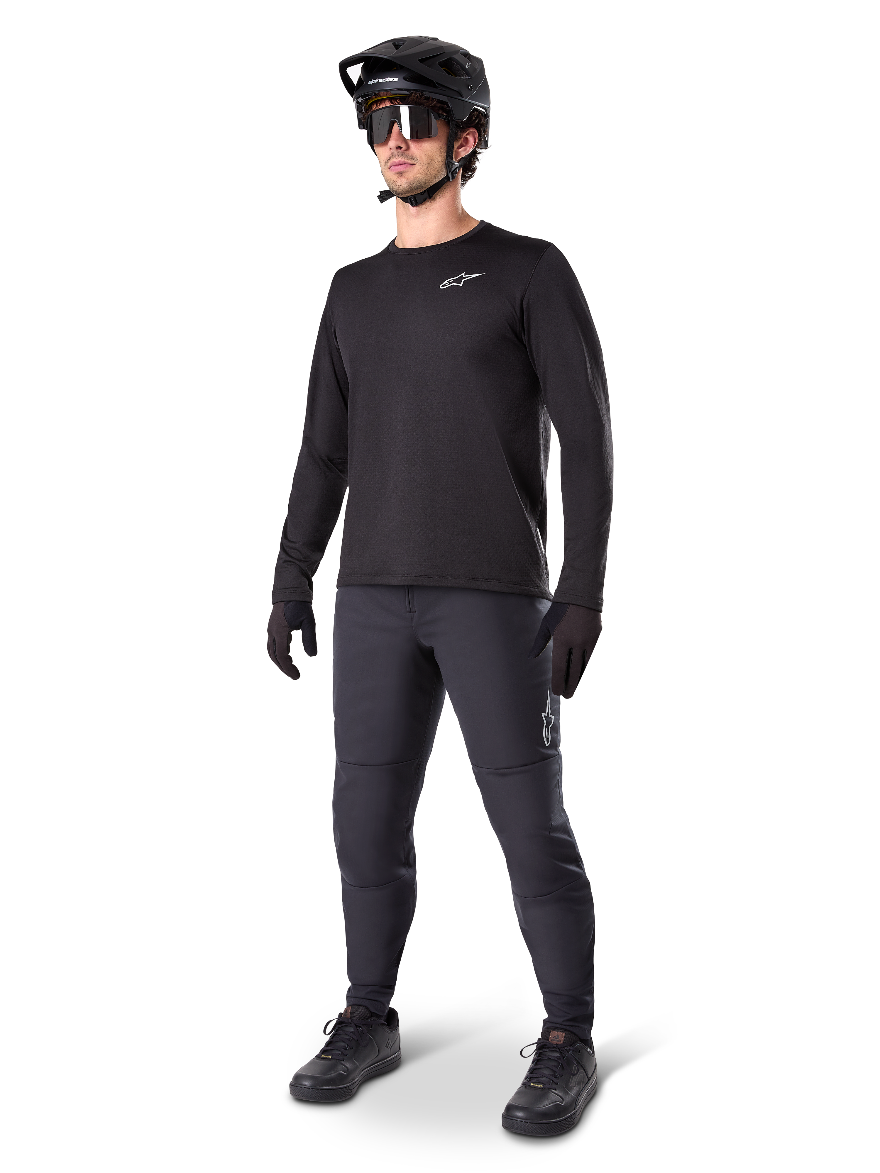 Ciclista di mountain bike che indossa i Pantaloni Termici Alpinestars A-Dura, nero, abbinati a una maglia a maniche lunghe nera, casco nero e occhiali da sole, con logo Alpinestars argento sulla coscia sinistra, progettati per il trail riding in climi freddi