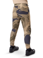 Alpinestars A-Dura Camo Pant, pantaloni MTB, motivo mimetico marrone con accenti sabbia e grigio scuro, vista posteriore con sneaker nere, gambe affusolate e polsini elasticizzati, tessuto resistente elasticizzato in 2 direzioni per mountain bike