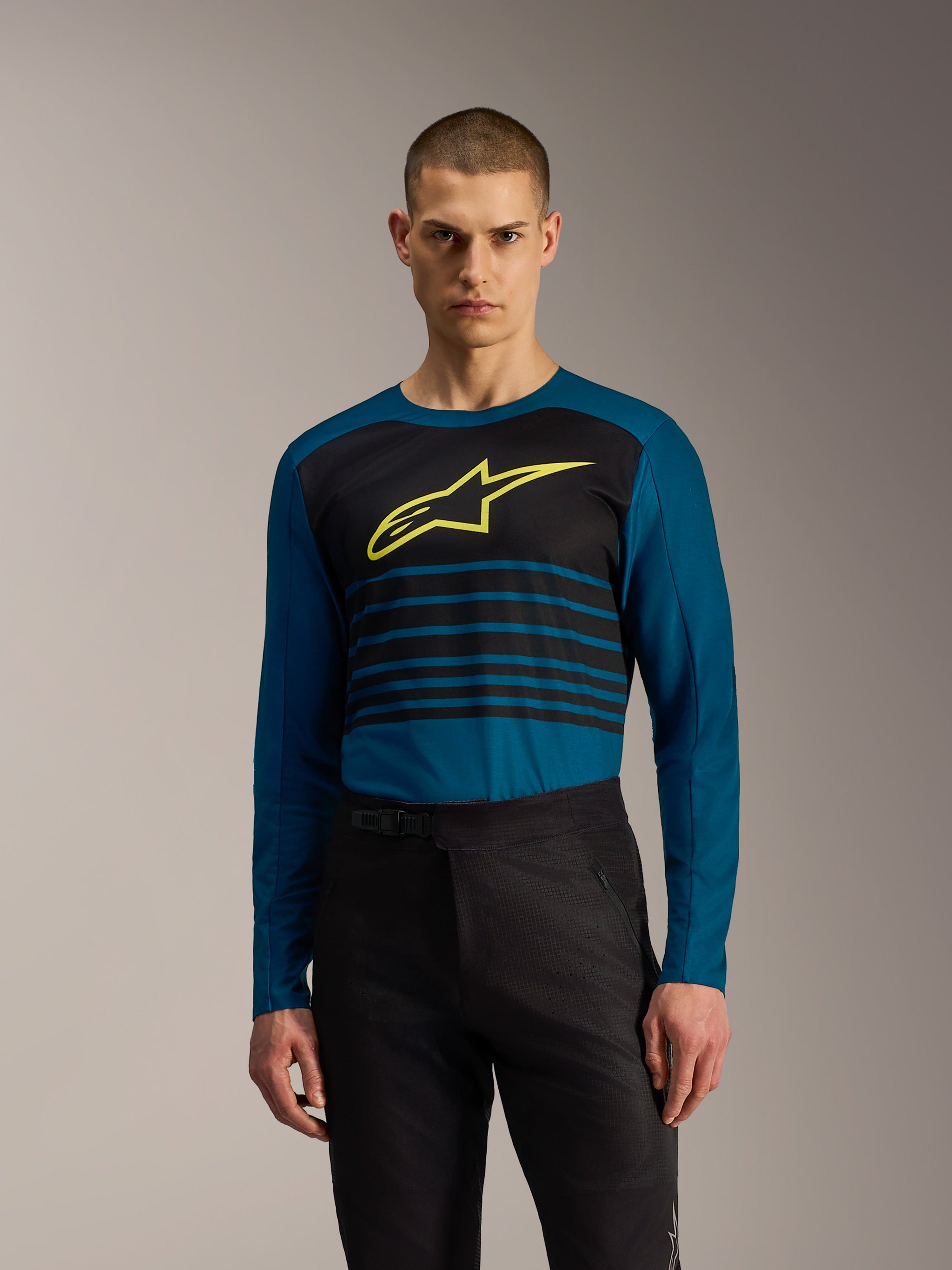 Pantaloni Alpinestars A-Dura Elite Flex neri abbinati a una maglia MTB blu a maniche lunghe e logo giallo.