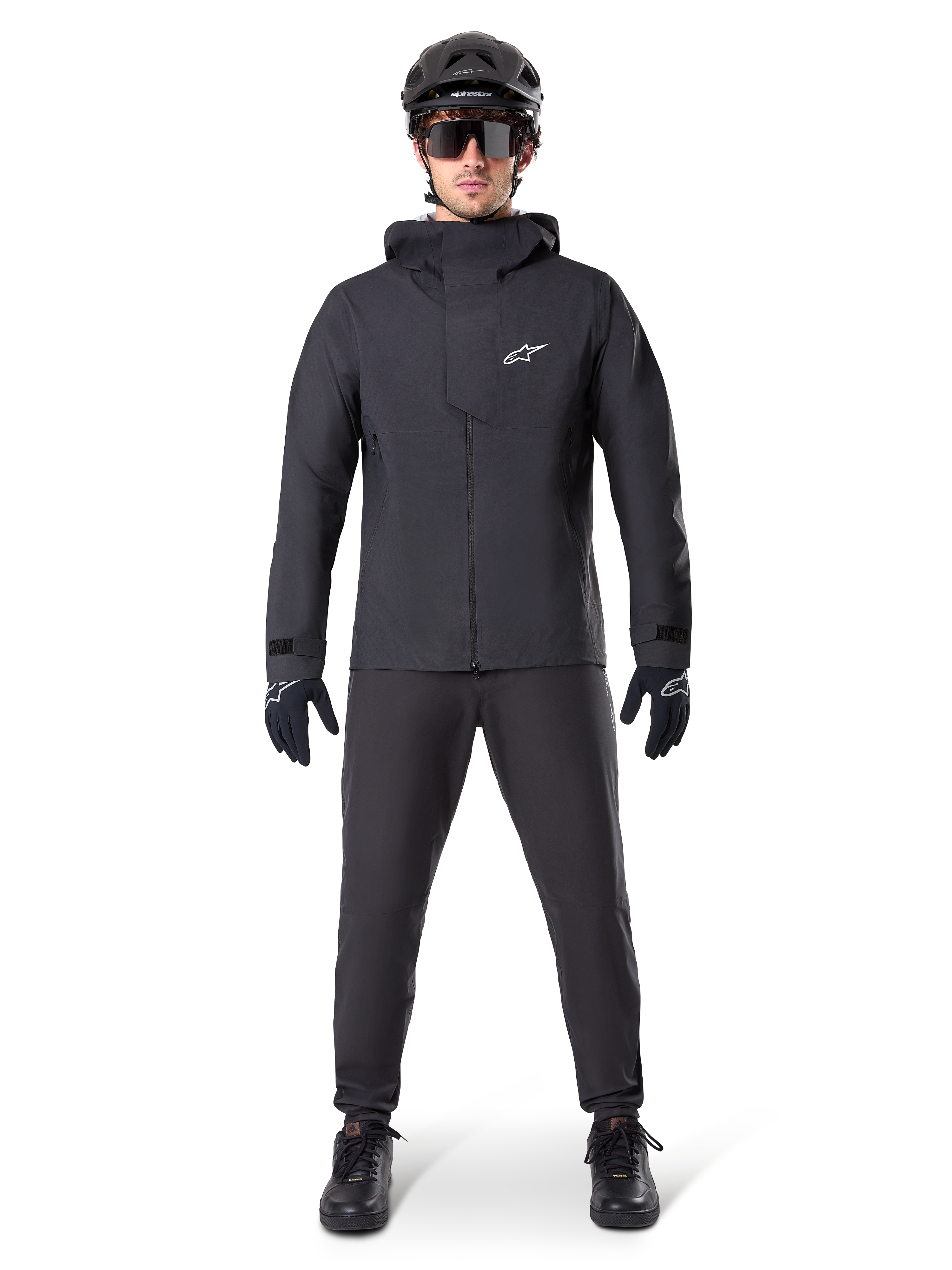 Pantaloni impermeabili Alpinestars A-Dura, pantaloni da MTB neri, indossati come parte di un set completo di abbigliamento da mountain bike total black che include giacca tecnica impermeabile, casco nero, occhiali da sole e guanti, progettati per la guida fuoristrada in condizioni di pioggia.