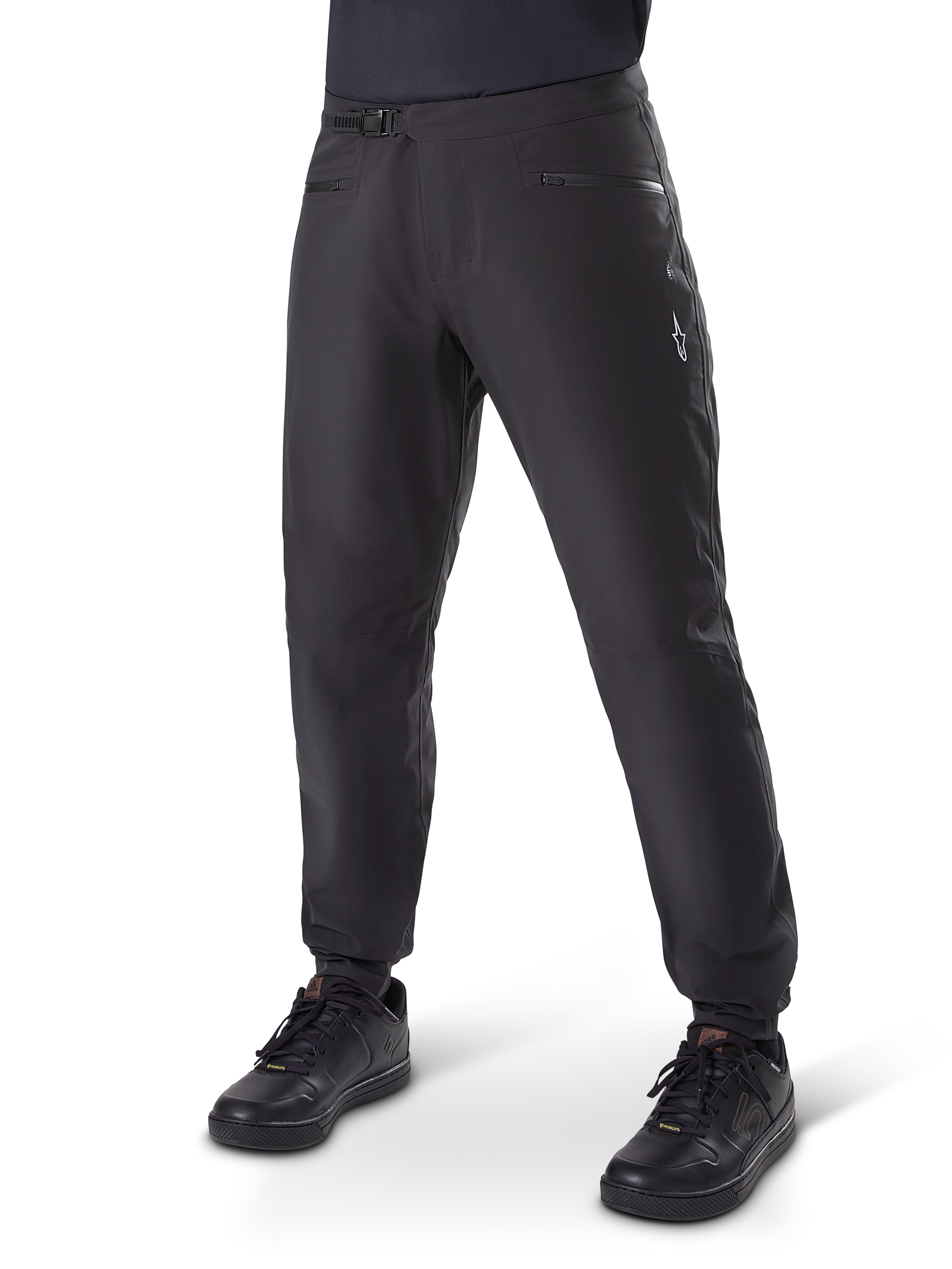 Alpinestars A-Dura Waterproof Pants, pantaloni da ciclismo MTB, nero, con chiusura a cricchetto in vita, tasche con cerniera e logo Astars bianco sulla coscia, mostrati con scarpe da ciclismo nere per il trail riding in ogni condizione meteorologica