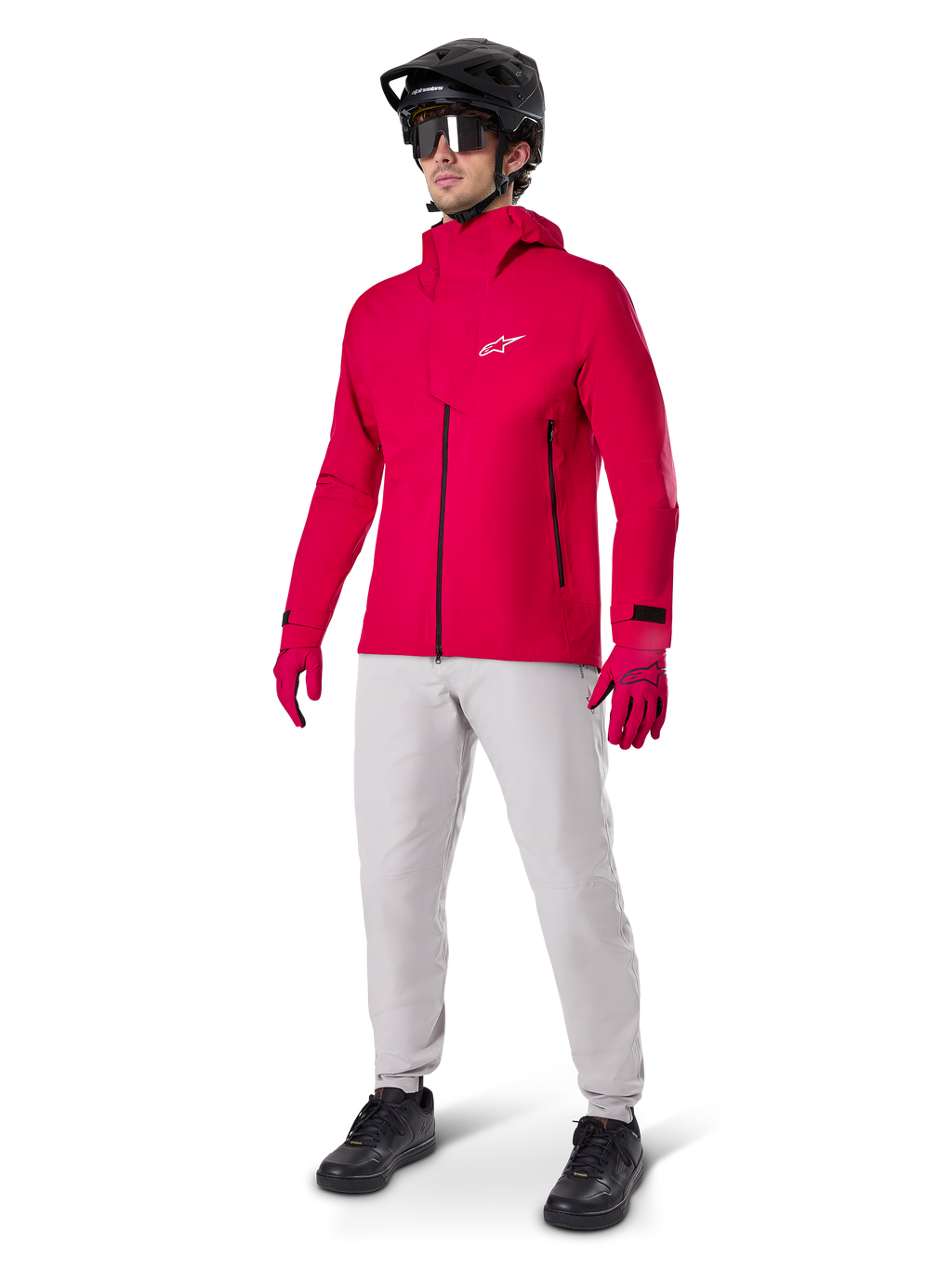 Modello che indossa i pantaloni impermeabili Alpinestars A-Dura in grigio Titanium, abbinati a una giacca impermeabile rosso acceso e guanti coordinati, casco da mountain bike nero con maschera e scarpe nere, abbigliamento completo da mountain bike per condizioni di sentieri bagnati