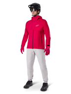 Modello che indossa i pantaloni impermeabili Alpinestars A-Dura in grigio Titanium, abbinati a una giacca impermeabile rosso acceso e guanti coordinati, casco da mountain bike nero con maschera e scarpe nere, abbigliamento completo da mountain bike per condizioni di sentieri bagnati