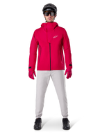 Pantaloni impermeabili Alpinestars A-Dura, pantaloni da MTB, grigio titanio, indossati con una giacca con cappuccio rosso vivace, guanti rossi e un casco da mountain bike nero, abbigliamento tecnico impermeabile professionale per percorsi bagnati