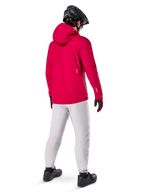 Pantaloni impermeabili Alpinestars A-Dura in Titanium, vista posteriore di un rider che indossa i pantaloni tecnici da mountain bike grigio chiaro con una giacca rossa con cappuccio e casco nero, abbigliamento impermeabile e resistente per il ciclismo in condizioni di bagnato