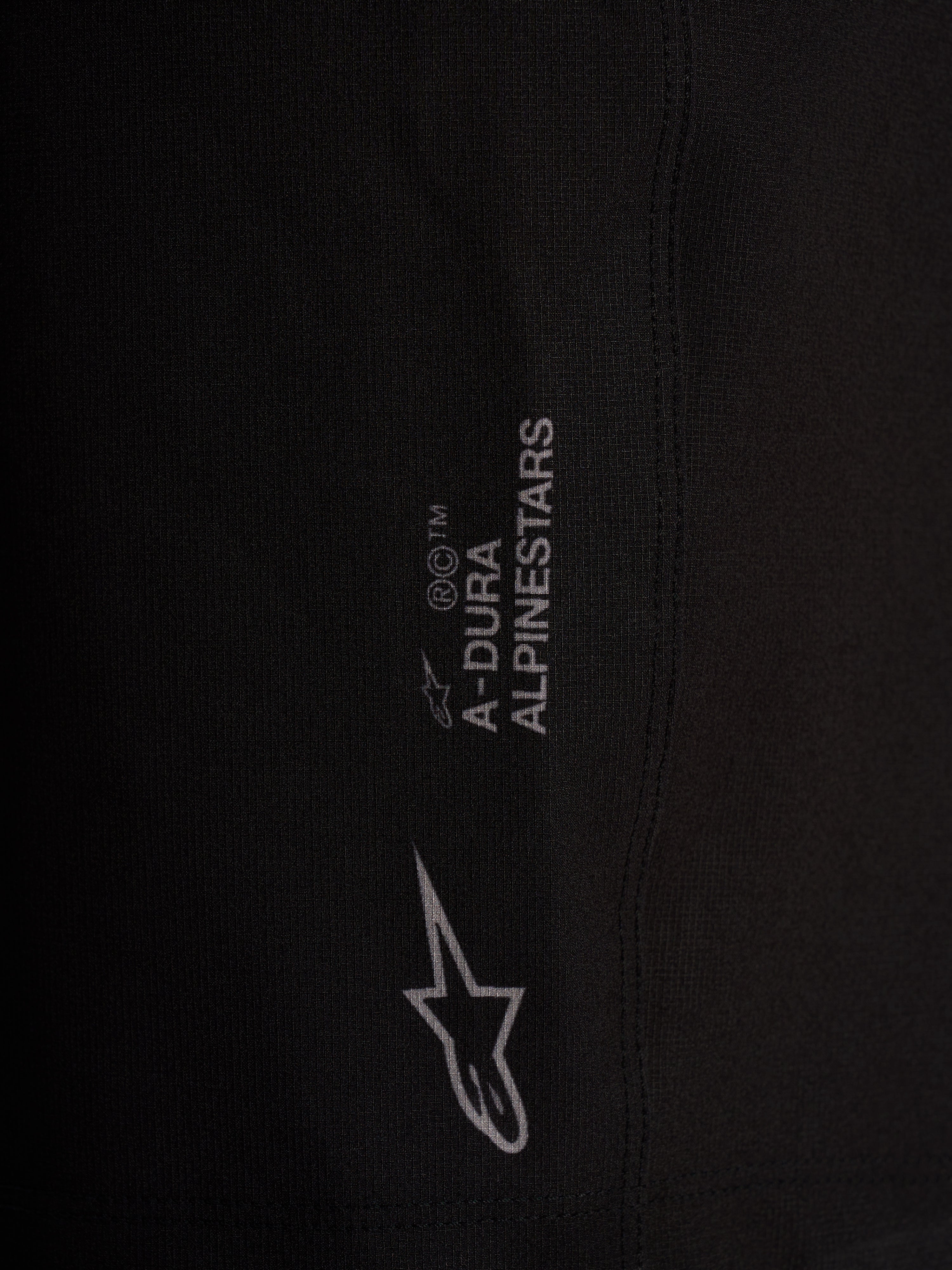 Dettaglio pantaloncini Alpinestars A-Dura Ride neri, tessuto tecnico elasticizzato a 4 vie con loghi bianchi.