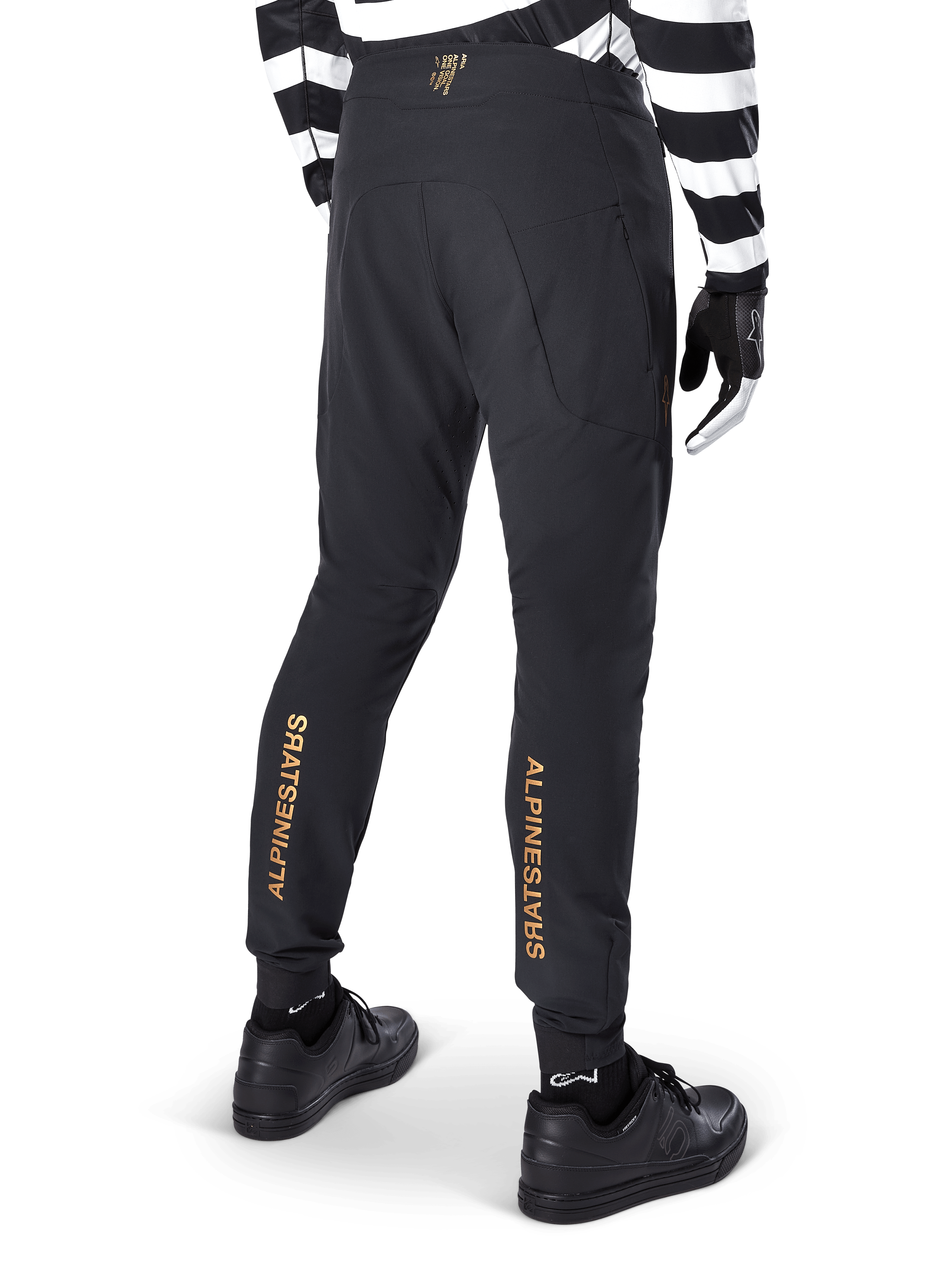 Pantaloni Alpinestars A-Aria Elite, pantaloni MTB neri, vista posteriore, con marchio Alpinestars dorato verticale sul retro delle gambe, indossati con una maglia a righe bianche e nere e scarpe nere, abbigliamento tecnico da ciclismo per mountain bike
