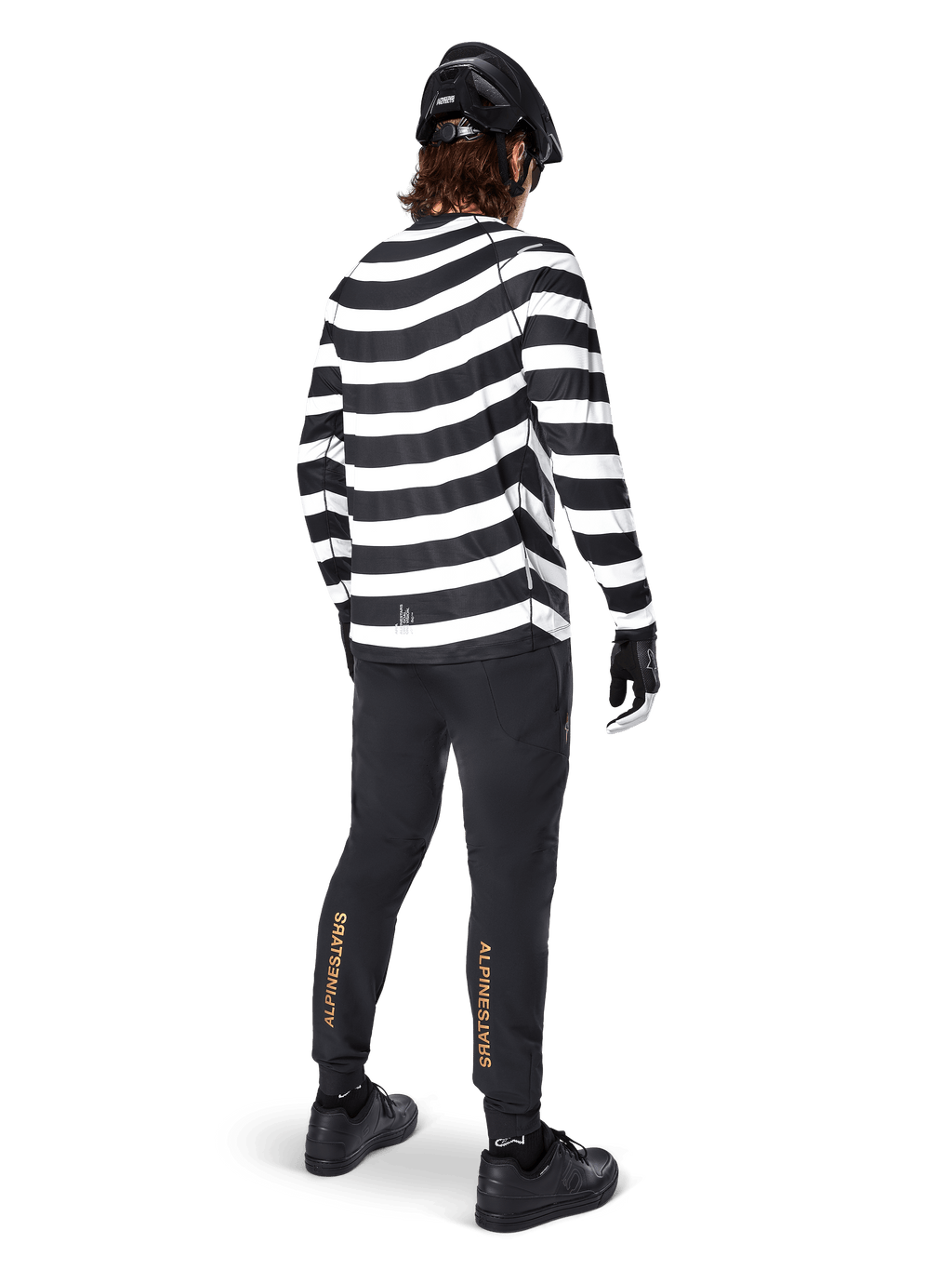 Pantaloni Alpinestars A-Aria Elite, pantaloni da MTB neri, con logo verticale dorato sui polpacci, indossati da un rider con maglia a maniche lunghe a righe bianche e nere, casco nero e scarpe nere, vista posteriore che mostra la vestibilità performante e il design pronto per il trail
