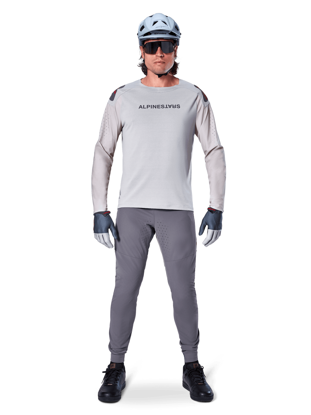 Pantaloni Alpinestars A-Aria Elite, pantaloni da mountain bike grigio scuro, indossati da un ciclista con maglia a maniche lunghe grigio chiaro, casco azzurro e scarpe nere, con perforazioni laser visibili nell'interno gamba e vestibilità slim da prestazione.