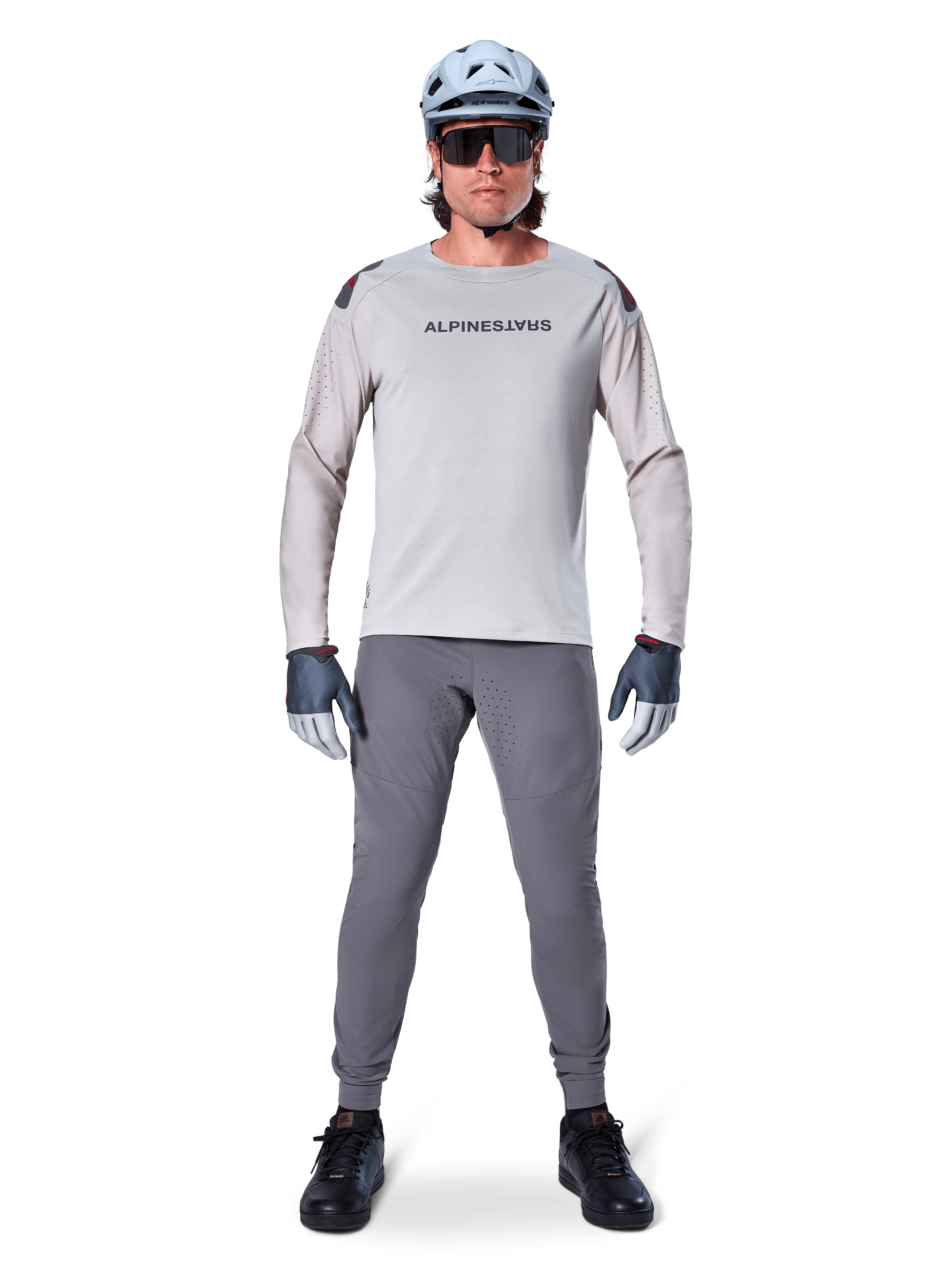 Pantaloni Alpinestars A-Aria Elite, pantaloni da mountain bike grigio scuro, indossati da un ciclista con maglia a maniche lunghe grigio chiaro, casco azzurro e scarpe nere, con perforazioni laser visibili nell'interno gamba e vestibilità slim da prestazione.