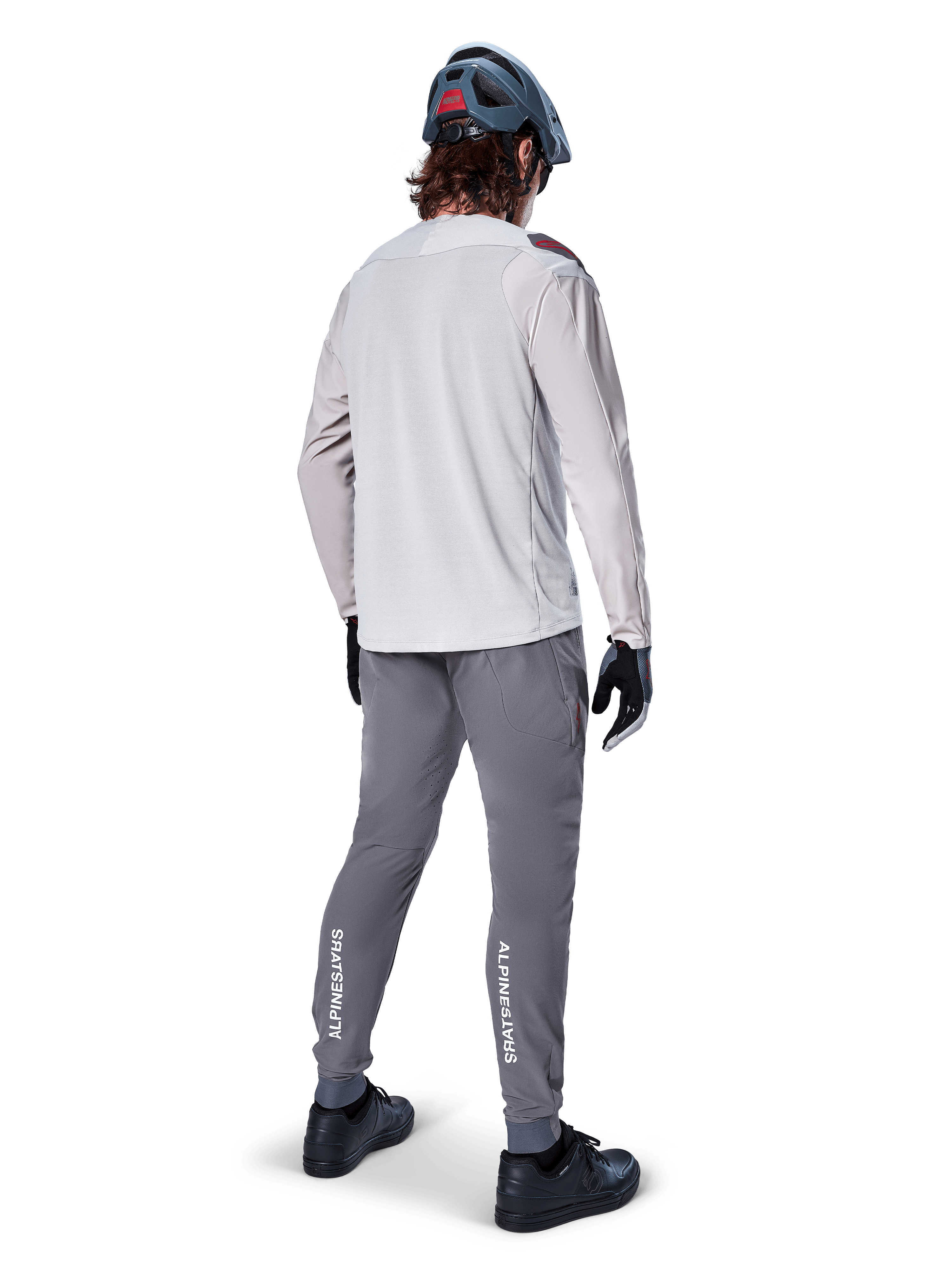 Pantaloni Alpinestars A-Aria Elite, pantaloni da ciclismo MTB, grigio scuro, vista posteriore di un rider con outfit completo, con marchio Alpinestars bianco sulla parte inferiore delle gambe, vestibilità performante con perforazioni laser, abbinati a una maglia a maniche lunghe grigio chiaro e casco da MTB grigio