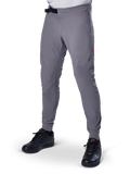 Alpinestars A-Aria Elite Pants, pantaloni da MTB grigio scuro, pannelli traforati al laser sulle cosce, chiusura con fibbia magnetica nera, tasca con zip, dettaglio logo rosso, vestibilità slim performance, indossati con scarpe nere