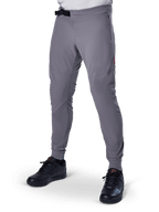Alpinestars A-Aria Elite Pants, pantaloni da MTB grigio scuro, pannelli traforati al laser sulle cosce, chiusura con fibbia magnetica nera, tasca con zip, dettaglio logo rosso, vestibilità slim performance, indossati con scarpe nere