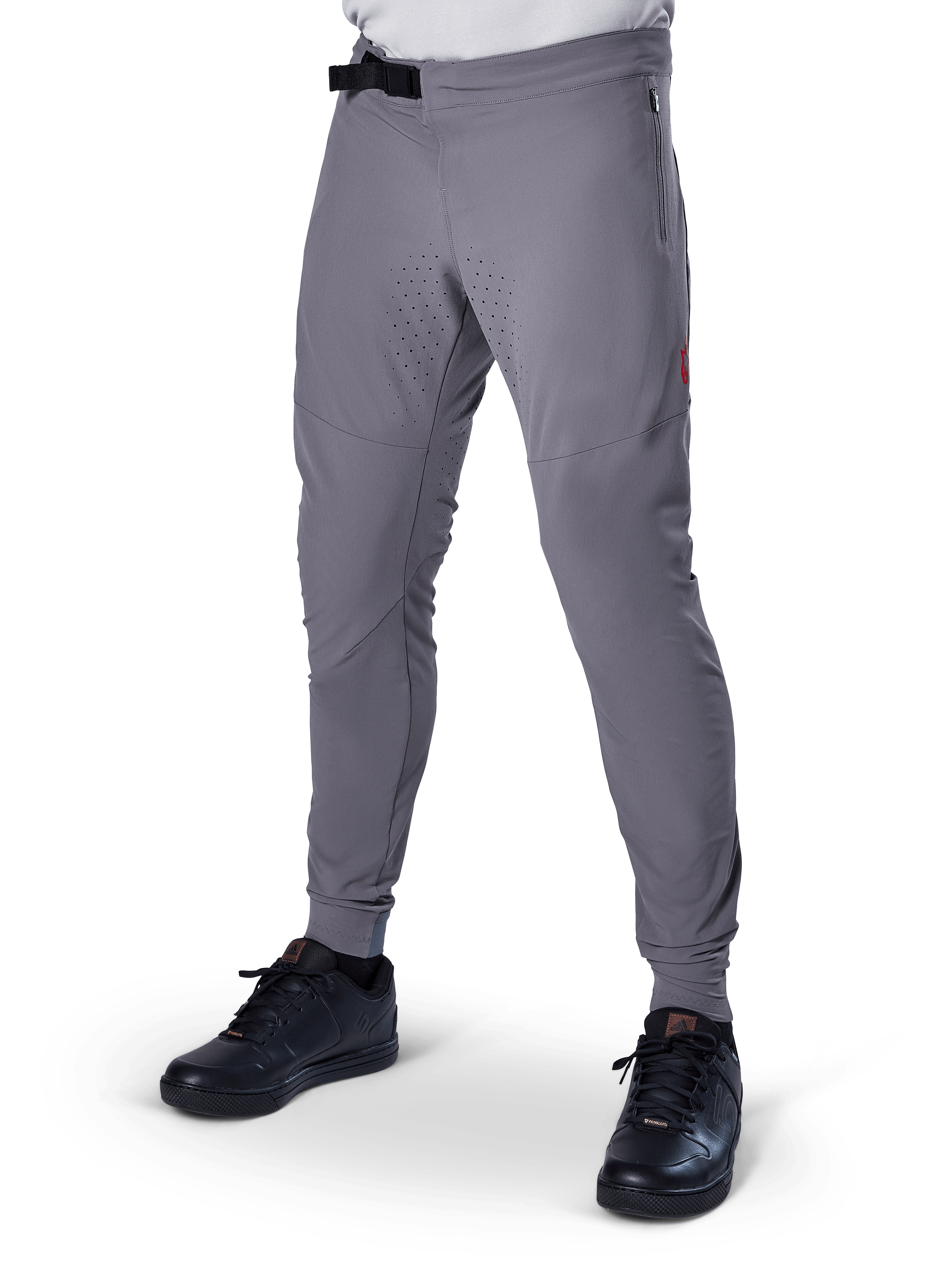 Alpinestars A-Aria Elite Pants, pantaloni da MTB grigio scuro, pannelli traforati al laser sulle cosce, chiusura con fibbia magnetica nera, tasca con zip, dettaglio logo rosso, vestibilità slim performance, indossati con scarpe nere