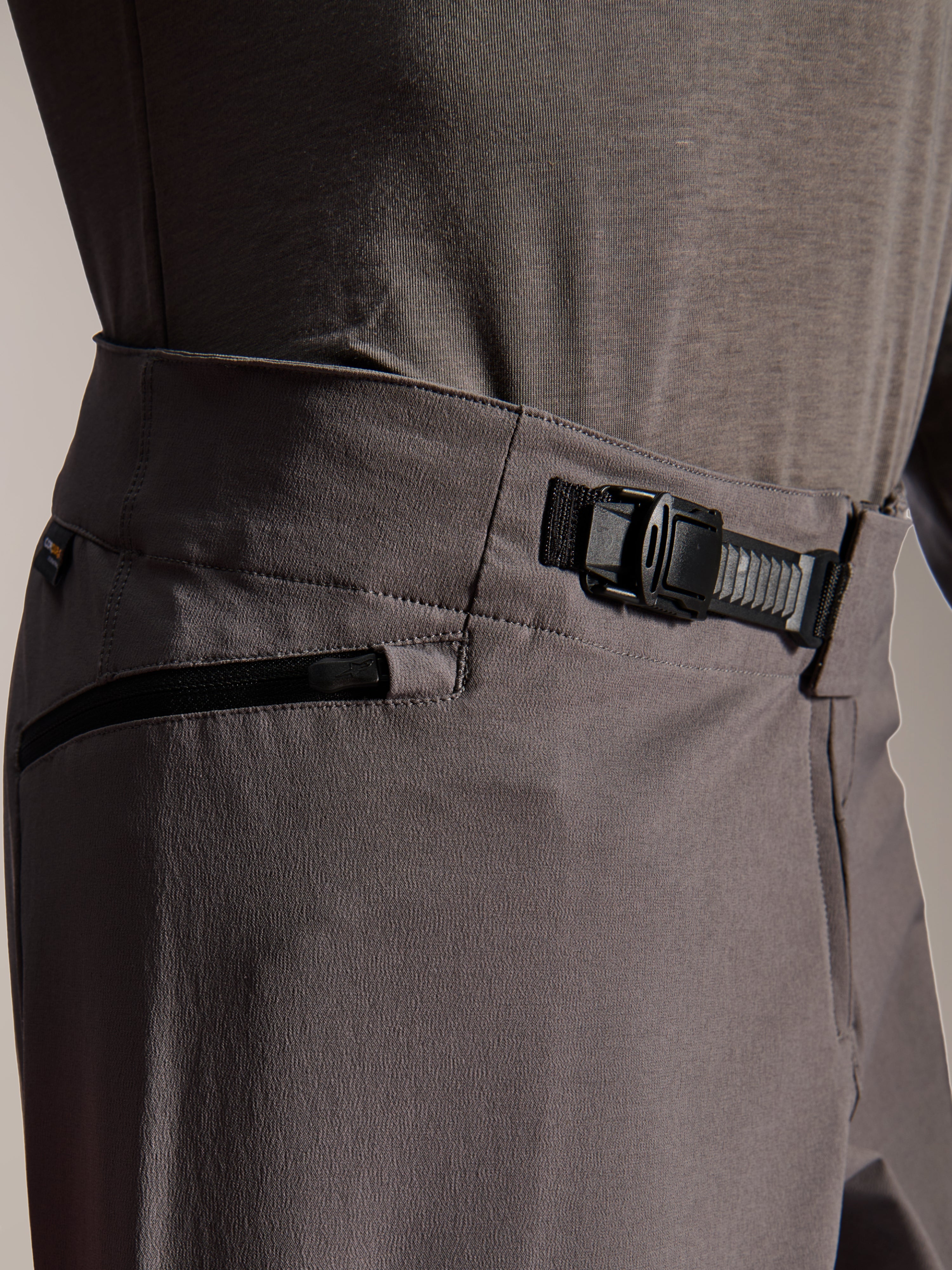 Alpinestars A-Dura Elite Pants, pantaloni MTB, grigio scuro, vista ravvicinata che mostra il sistema di chiusura a cricchetto anteriore e la tasca con zip, abbigliamento tecnico per mountain bike