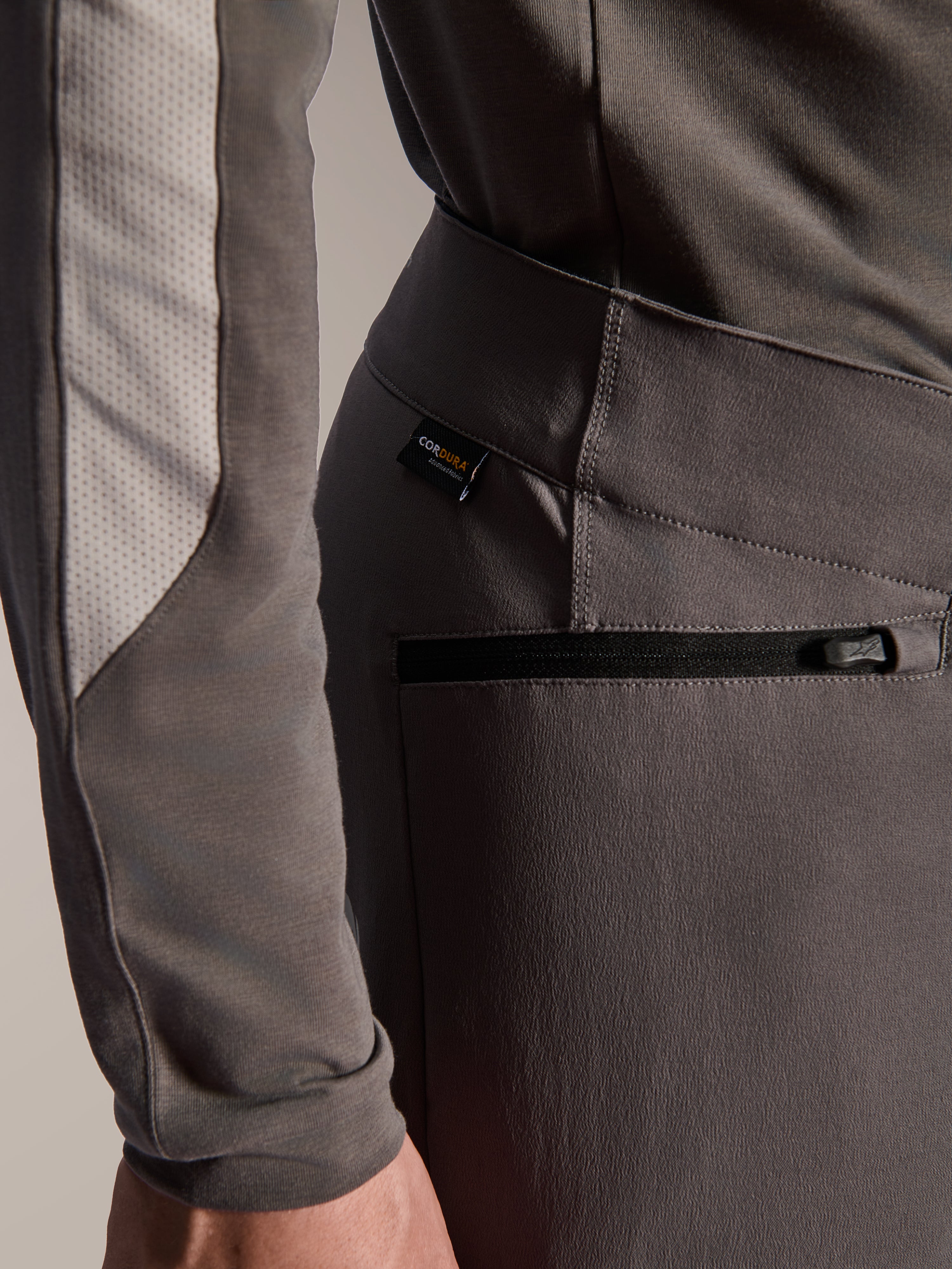 Alpinestars Pantaloni A-Dura Elite, pantaloni da mountain bike grigio scuro, dettaglio ravvicinato della tasca laterale con zip e dell'etichetta in tessuto Cordura, tessuto resistente elasticizzato in 4 direzioni per prestazioni off-road