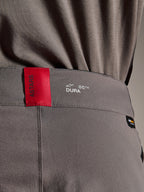 Alpinestars A-Dura Elite Pants, pantaloni da MTB, grigio scuro, primo piano della fascia in vita con etichetta rossa ASTARS e logo bianco DURA, tessuto Cordura testurizzato e dettagli di branding premium.