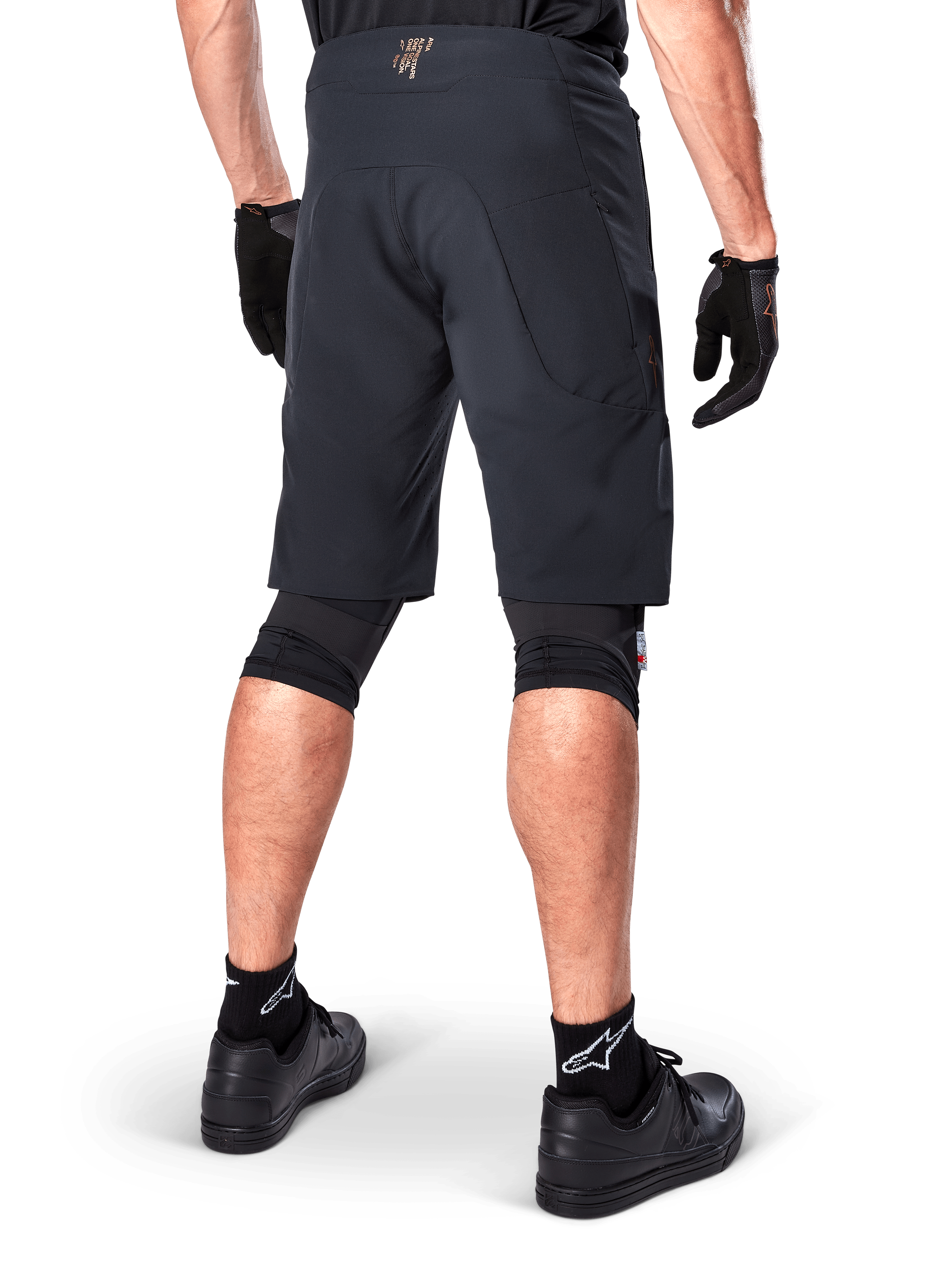 Vista posteriore di un rider che indossa i pantaloncini Alpinestars A-Aria Elite in nero, pantaloncini da mountain bike ad alte prestazioni, abbinati a guanti da ciclismo neri e scarpe nere, progettati per la flessibilità di movimento su percorsi fuoristrada