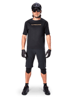 Ciclista di mountain bike con pantaloncini Alpinestars A-Aria Elite neri, abbinati a maglia a maniche corte coordinata, casco, guanti e ginocchiere neri, outfit completo per ciclismo fuoristrada
