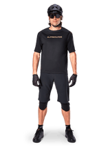 Male mountain bike rider wearing Alpinestars A-Aria Elite Shorts in Black, paired with a matching black Alpinestars short-sleeve jersey, black helmet, gloves, and knee guards, complete off-road cycling gear outfit