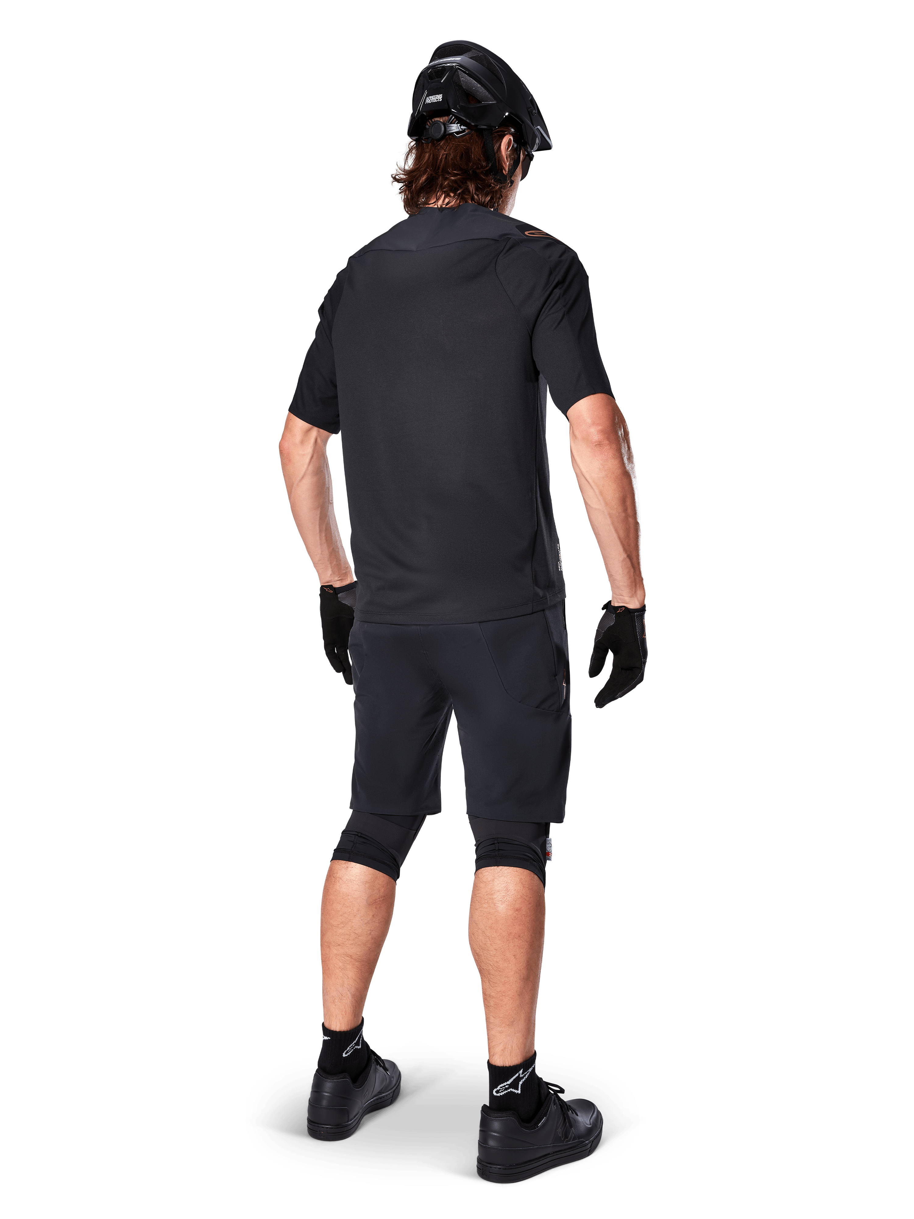 Vista posteriore di un mountain biker che indossa i pantaloncini Alpinestars A-Aria Elite neri, abbinati a una maglia a maniche corte coordinata, casco nero, guanti e scarpe da MTB, che mostra un outfit tecnico completo per il ciclismo off-road.