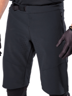 Pantaloncini Alpinestars A-Aria Elite in nero, vista ravvicinata della zona vita e coscia, con chiusura a fibbia magnetica, tasche con zip e perforazioni di ventilazione tagliate al laser, indossati con guanti da ciclismo neri per mountain bike.
