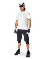 Mountain biker uomo con pantaloncini Alpinestars A-Aria, pantaloncini da ciclismo neri, abbinati a una maglia bianca a maniche corte, casco da mountain bike bianco e attrezzatura tecnica nera, outfit completo per il trail riding fuoristrada